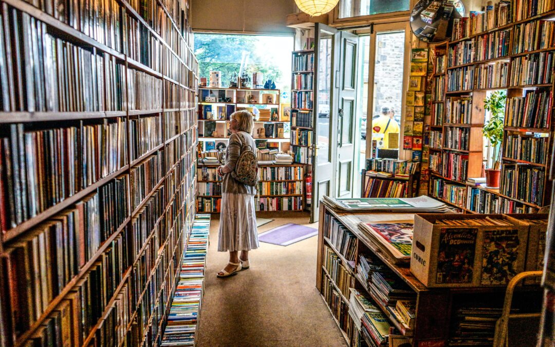 Image of a bookstore interior with a women grabbing a book off of a shelf.