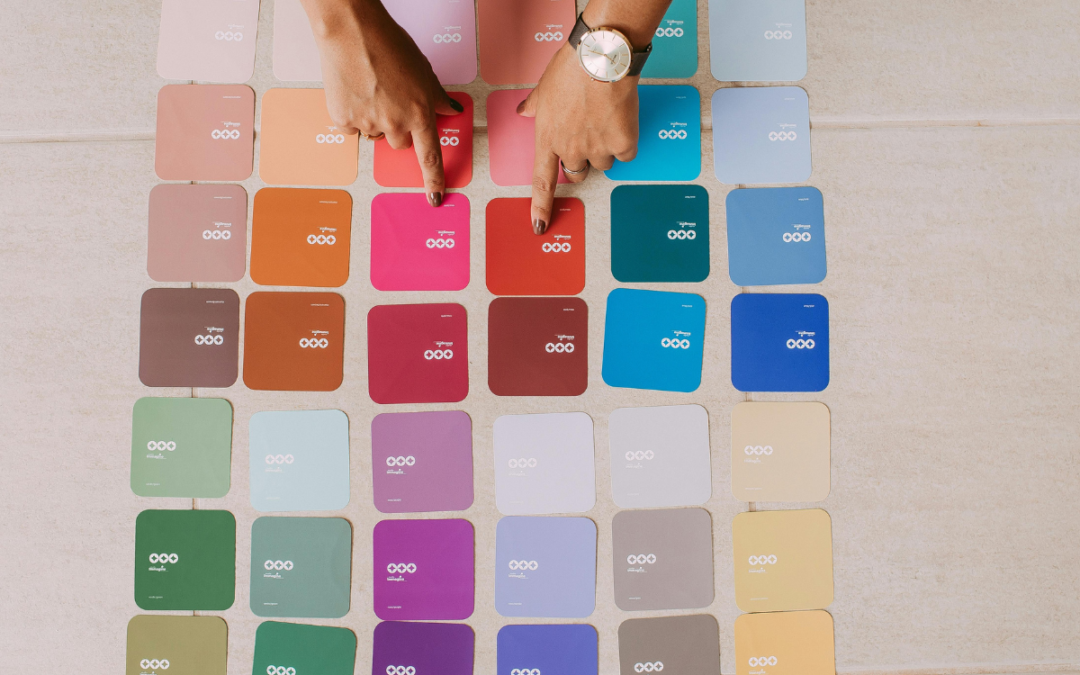 Paint color samples laid out on the ground with hands pointing to them to represent choosing the color theme of your website.